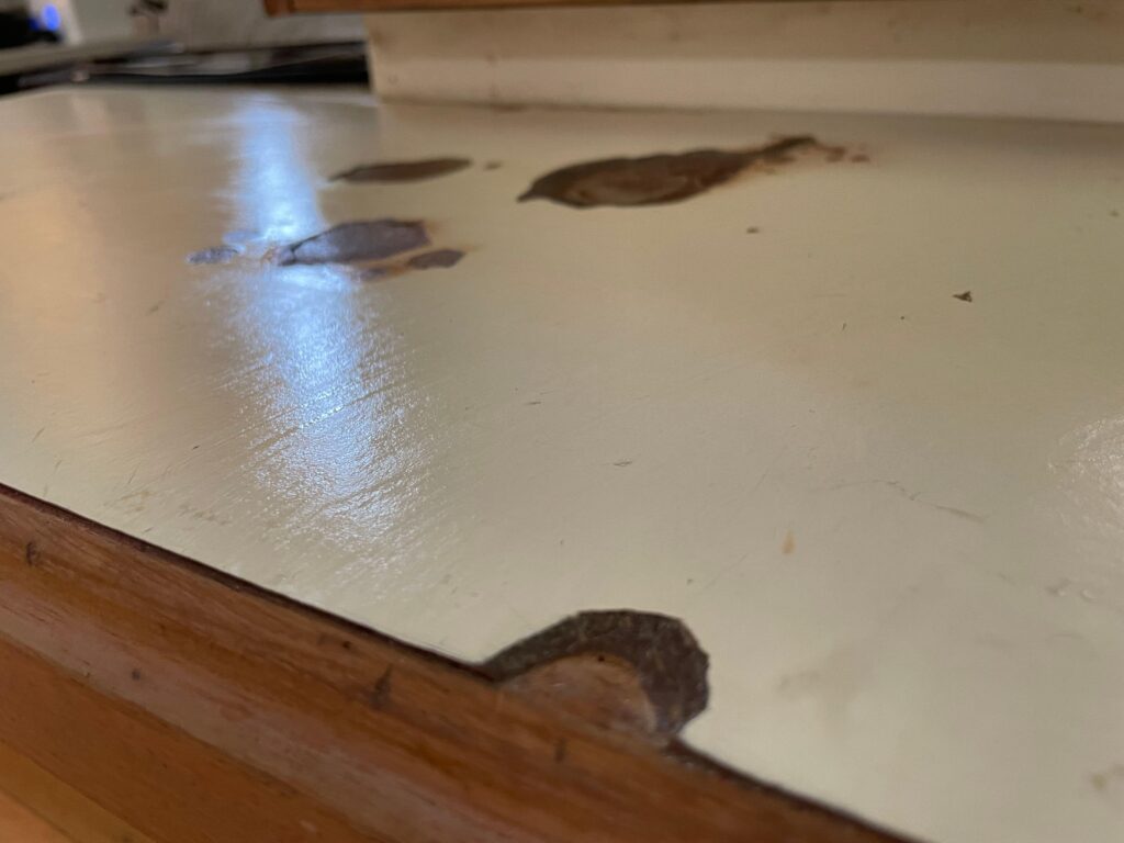 Kitchen countertop with chipped edges, deep scratches, and surface damage requiring replacement.