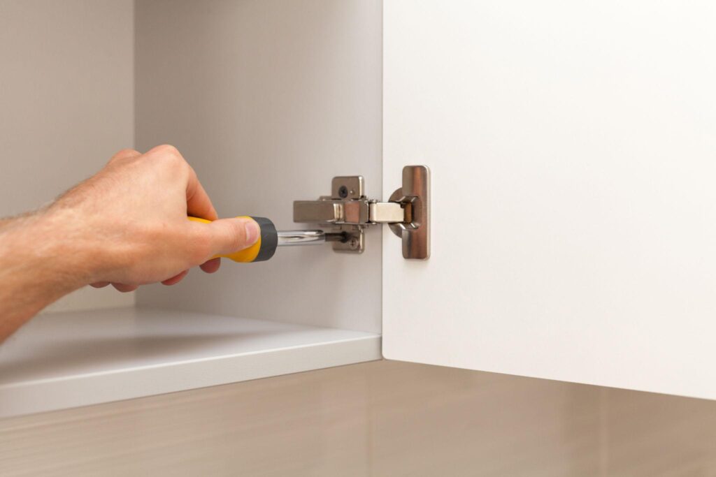 Homeowner repairing damaged kitchen cabinet hinges and worn cabinet doors
