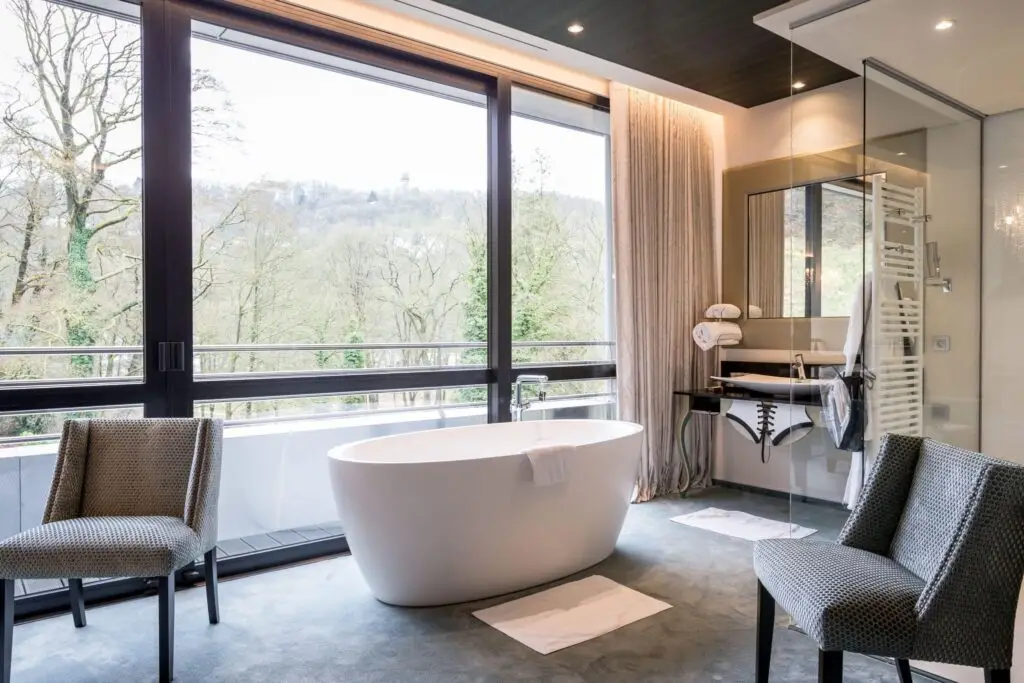 Luxury bathroom with a freestanding soaking tub overlooking a landscaped garden through floor-to-ceiling windows